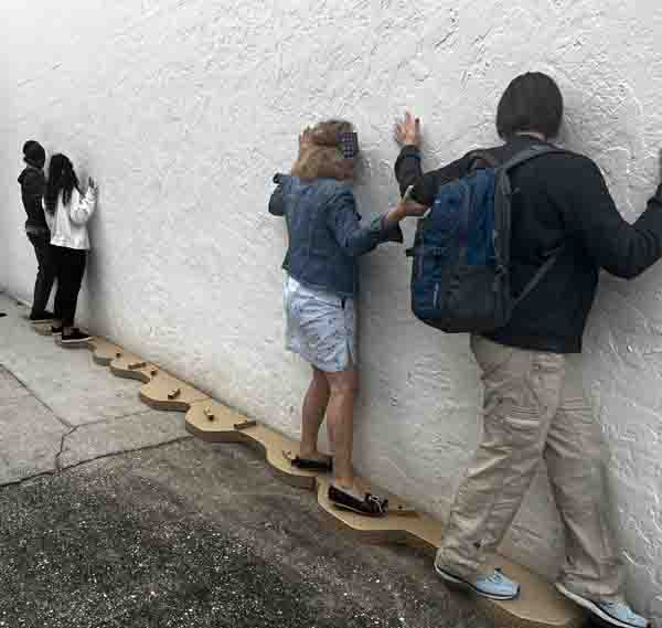  two pairs of participants are pressed up against a wall, facing the wall and side-stepping along a one-foot-wide strip of panels, with blocks randomly attached.
